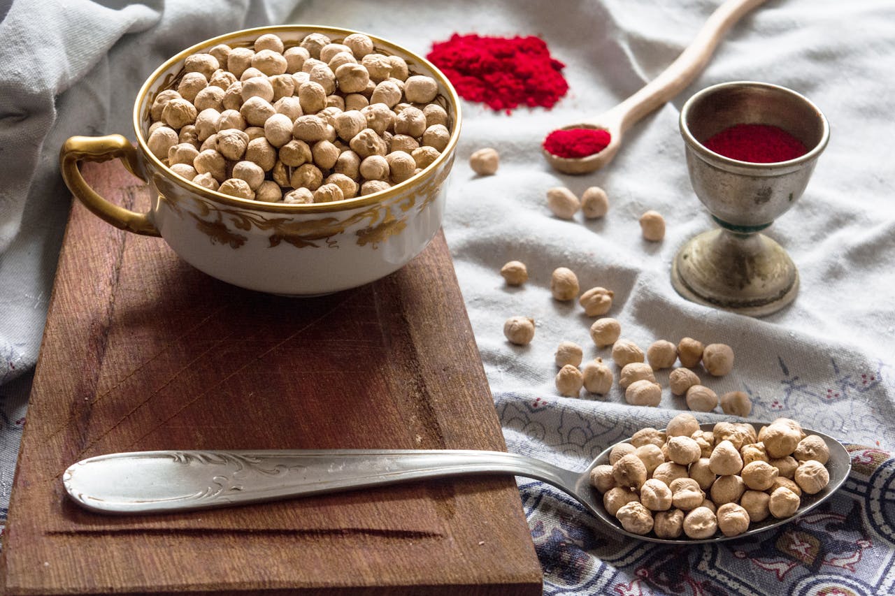 gallery-4 Chickpeas in a cup on a wooden board with spices, showcasing a rustic food preparation setup.