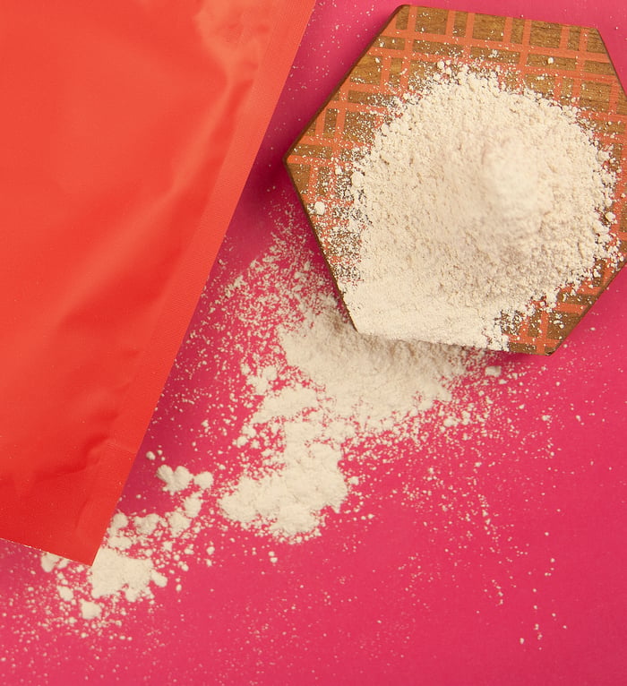 services-03 White flour spilled from a red bag onto a pink surface, viewed from above.